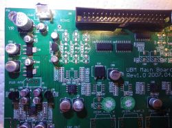 Nahaufnahme einer grünen Leiterplatte mit verschiedenen elektronischen Bauteilen und Markierungen.