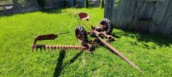 Old horse-drawn mower with large wheels and cutting bar on grass near wooden shed