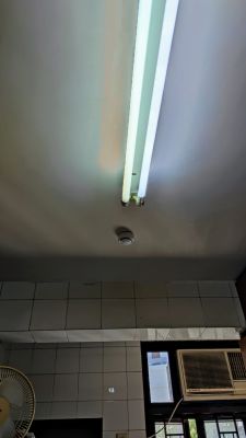 Smoke detector installed on a kitchen ceiling with a fluorescent light.