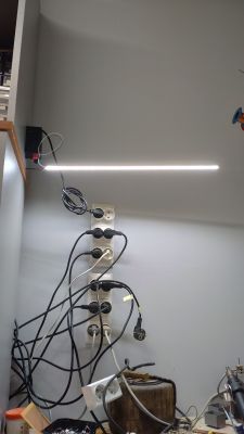 Świetlówka LED zamontowana na ścianie, z licznymi kablami i wtyczkami podłączonymi do gniazdek.