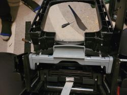 Interior of a black plastic housing with a gray piece and springs; tools lie on the carpet behind