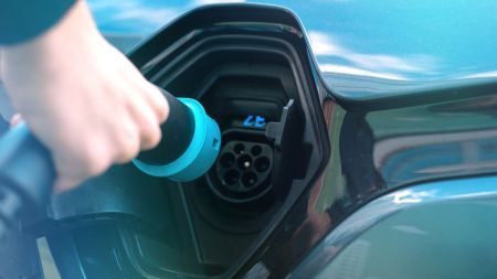 Ładowanie auta elektrycznego z bliska Ręka podłącza niebieską wtyczkę do gniazda ładowania samochodu elektrycznego