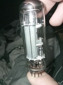 Rurka szklana z lampą elektronową trzymana w palcach, widoczne wewnętrzne elementy