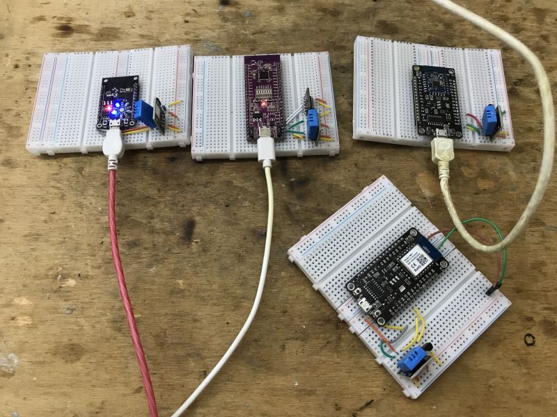 Four breadboards with microcontrollers and components on a wooden table.