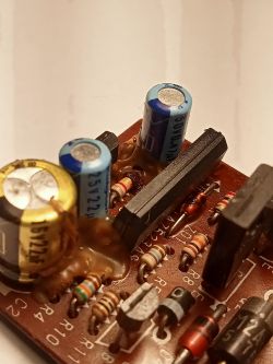 Zbliżenie na płytkę drukowaną z kilkoma kondensatorami elektrolitycznymi, na których widać brązową substancję wokół ich podstawy.