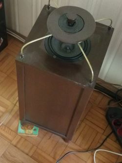 Speaker with two diffusers placed on a wooden floor next to a power strip.