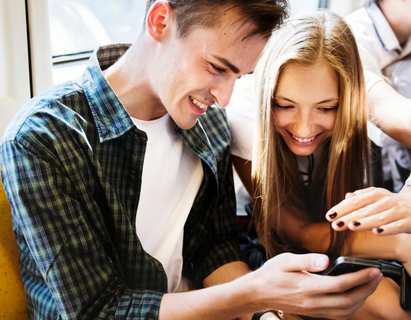 Mężczyzna i kobieta z uśmiechem patrzą na smartfon.