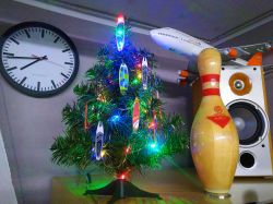 Weihnachtsbaum mit bunten Lichtern, neben einer Wanduhr und einem Flugzeugmodell.