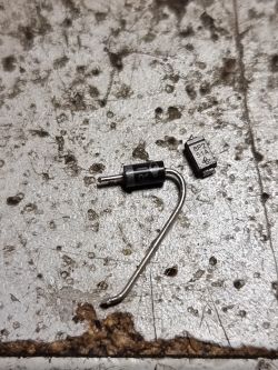 Dioda prostownicza SMD i komponent elektroniczny na zniszczonej powierzchni.