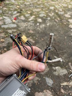 Osoba trzymająca wiązkę kabli z kontrolerem na tle kamiennej nawierzchni.