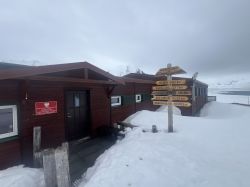 Polish Polar Station Hornsund with Signpost A wooden building of the Polish Polar Station Hornsund against a snowy landscape with a signpost indicating directions and distances to various locations.