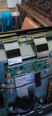 View of a TV interior showing a T-CON board and connection cables.