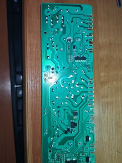 Płyta drukowana z urządzenia elektronicznego z widocznymi ścieżkami i punktami lutowniczymi na drewnianym tle.