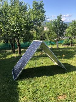 Panel słoneczny ustawiony w kształcie namiotu na trawniku w otoczeniu drzew.