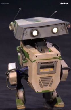 Mały robot na scenie z kamerą, prostokątną głową i świecącymi oczami