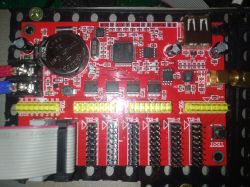 Czerwony obwód drukowany z elementami elektronicznymi, w tym kondensatory, bateria i złącza.