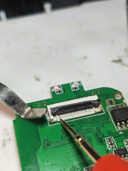 Close-up of FFC connector on green PCB with a measurement probe touching the pins
