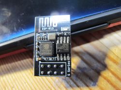 ESP-01S with replaced memory chip against a laptop background.