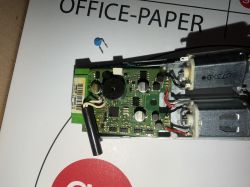 Płytka elektroniki z przewodami i dwoma silnikami DC w metalowej obudowie; obok wylutowany niebieski element
