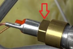 Zbliżenie na metalową cewkę elektrozaworu z czerwoną plastikową końcówką i zaznaczoną strzałką nakrętką.