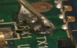 Close-up of a damaged circuit board with visible solder points labeled RX1 and TX1.