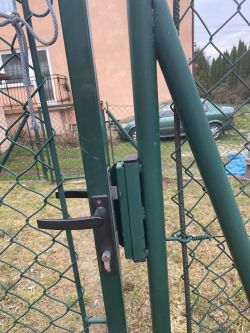 Zbliżenie na zieloną bramę z siatki, wyposażoną w elektrozaczep i klamkę.