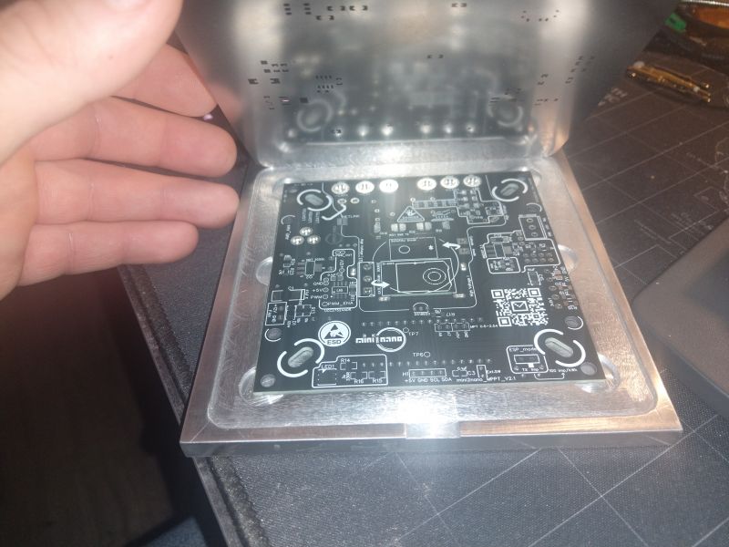 A person holding a metal stencil above a black PCB.