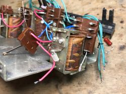 Close-up of a disassembled relay with coil, contacts, and loose wires on a wooden workbench