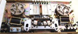 Open reel-to-reel tape recorder mechanism with reels, tape heads, and two analog meters