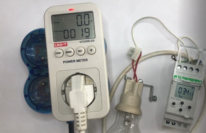 Miernik energii podłączony do gniazdka, żarówka i licznik energii elektrycznej.