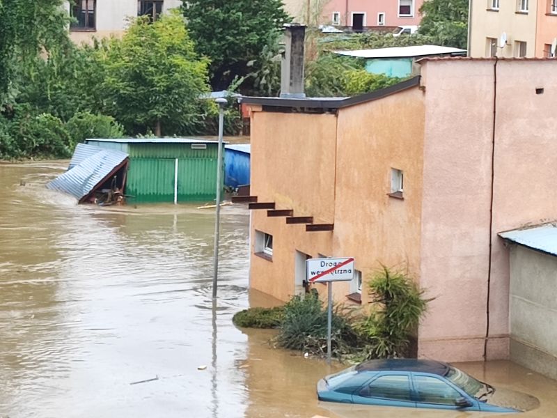 Zalana ulica z widocznym dachem samochodu i budynkiem w tle.