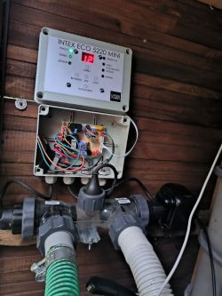 Przerobiony generator chloru Intex 5220 MINI zamontowany na ścianie z otwartą obudową, ukazującą połączenia elektryczne.