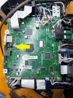 Zdjęcie ukazuje płytę główną z podłączonymi przewodami i elementami elektronicznymi, z zaznaczeniem żółtą strzałką.