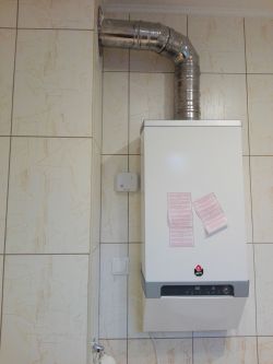 Wiszący kocioł gazowy na ścianie wyłożonej płytkami ceramicznymi z podłączoną rurą spalinową.