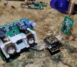 ESP8266 and CC1101 Modules Connected to Power Plug Circuit Close-up of an electronic circuit board with an attached ESP8266 module, a CC1101 radio module with a spiral antenna, and connecting wires.