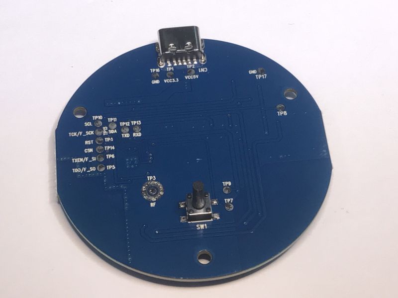 Bottom of a blue circular PCB with a button and labeled programming pins