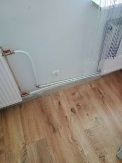Instalacja grzewcza na ścianie z gniazdkiem elektrycznym i podłogą z paneli drewnianych.