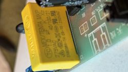 Żółty kondensator MEX/TENTA MKP X2 1,0 µF 275 VAC na płytce PCB, obok nadruku C1