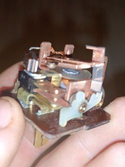 Zbliżenie na rękę trzymającą przekaźnik elektromagnetyczny z widocznymi miedzianymi elementami.