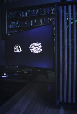 Zbliżenie na monitor komputerowy z widocznymi logotypami na ekranie, obok widoczna część obudowy komputera z podświetleniem.