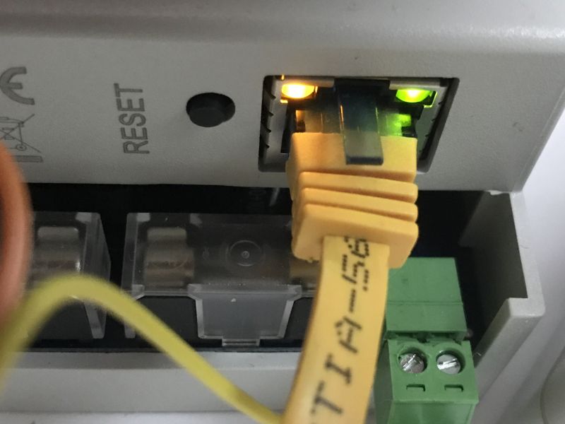 Close-up of an ethernet port with a connected yellow network cable, visible LEDs, and a RESET button.