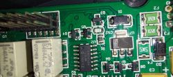 Zbliżenie na płytkę drukowaną z układami scalonymi, przekaźnikami i oznaczeniami elementów elektronicznych.
