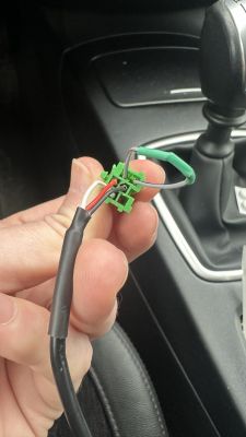 The image shows a hand holding a plug with wires in a car.