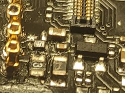 Zbliżenie na płytkę drukowaną z widocznymi elementami SMD, w tym oznaczenia F1 i inne.