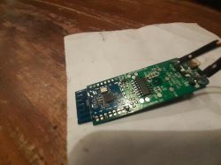 Close-up of a green-and-blue PCB with electronic components and attached wires on a white sheet of paper.