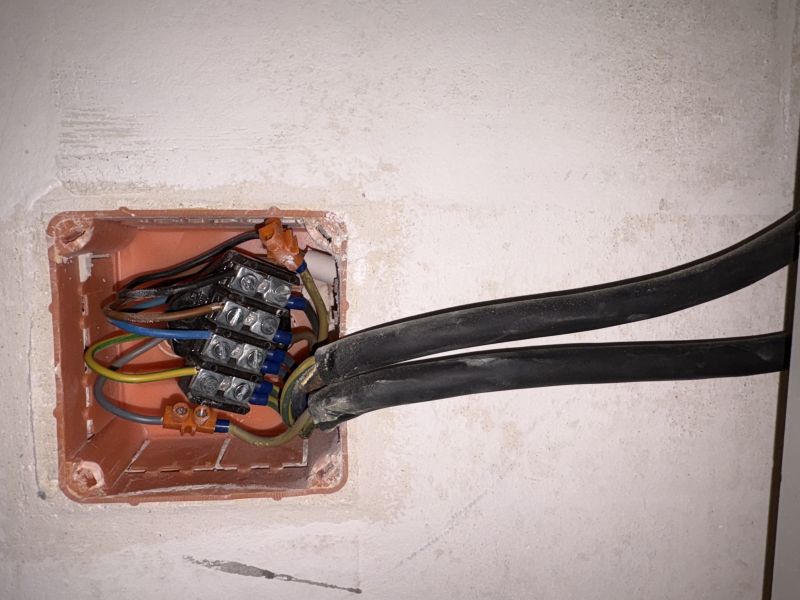 Otwarta puszka elektryczna w ścianie z listwą zaciskową i dwoma czarnymi przewodami