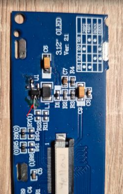 Close-up of a blue PCB with SMD parts and a red arrow pointing to a wire jumper.