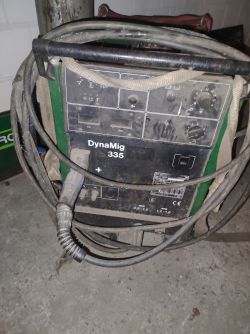 Stara spawarka DynaMig 335 z przewodami na tle betonowej podłogi.