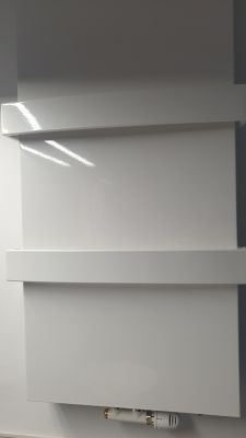 Biały grzejnik łazienkowy na tle białej ściany, z widocznym regulatorem temperatury na spodzie.