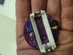 A purple printed circuit board with a white battery holder, held in a hand.
